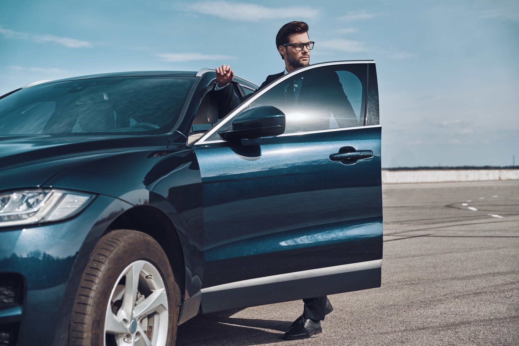 On the way to business meeting. Handsome young businessman entering his car while standing outdoors